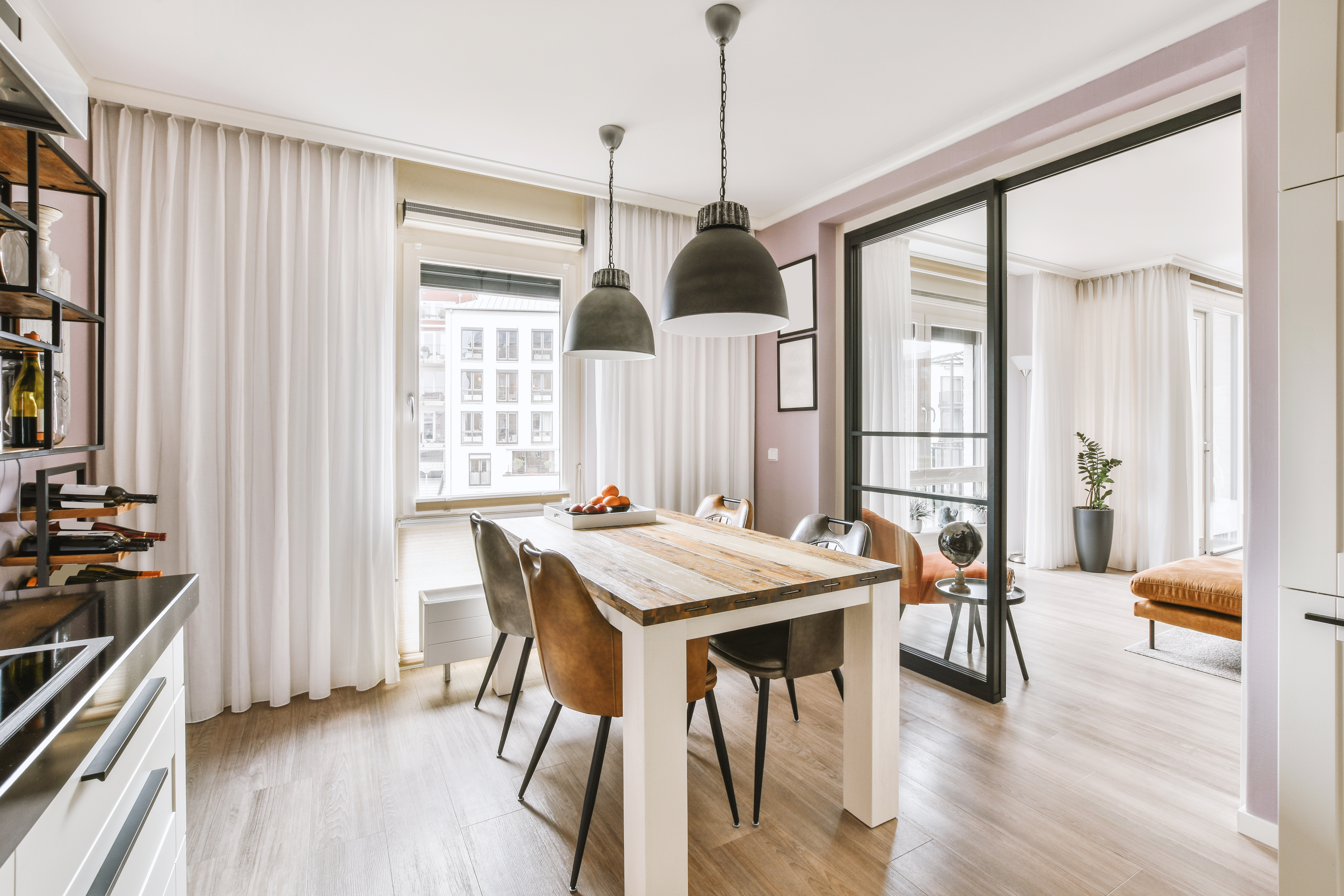 Modern kitchen and dining area with wooden table, pendant lights, and pink accent walls
