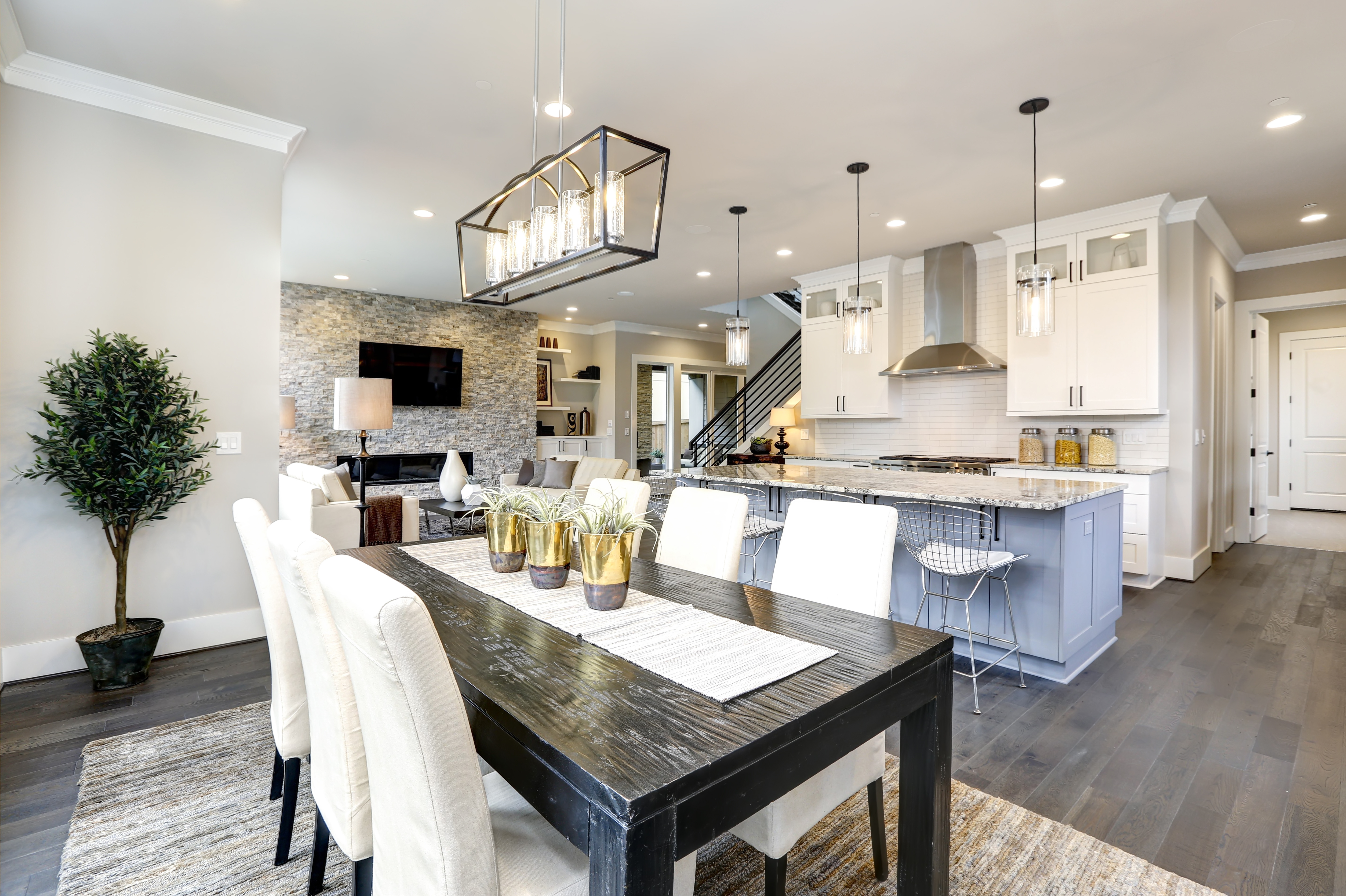 Modern open-concept home with dining table, kitchen island, white cabinetry, and stone fireplace