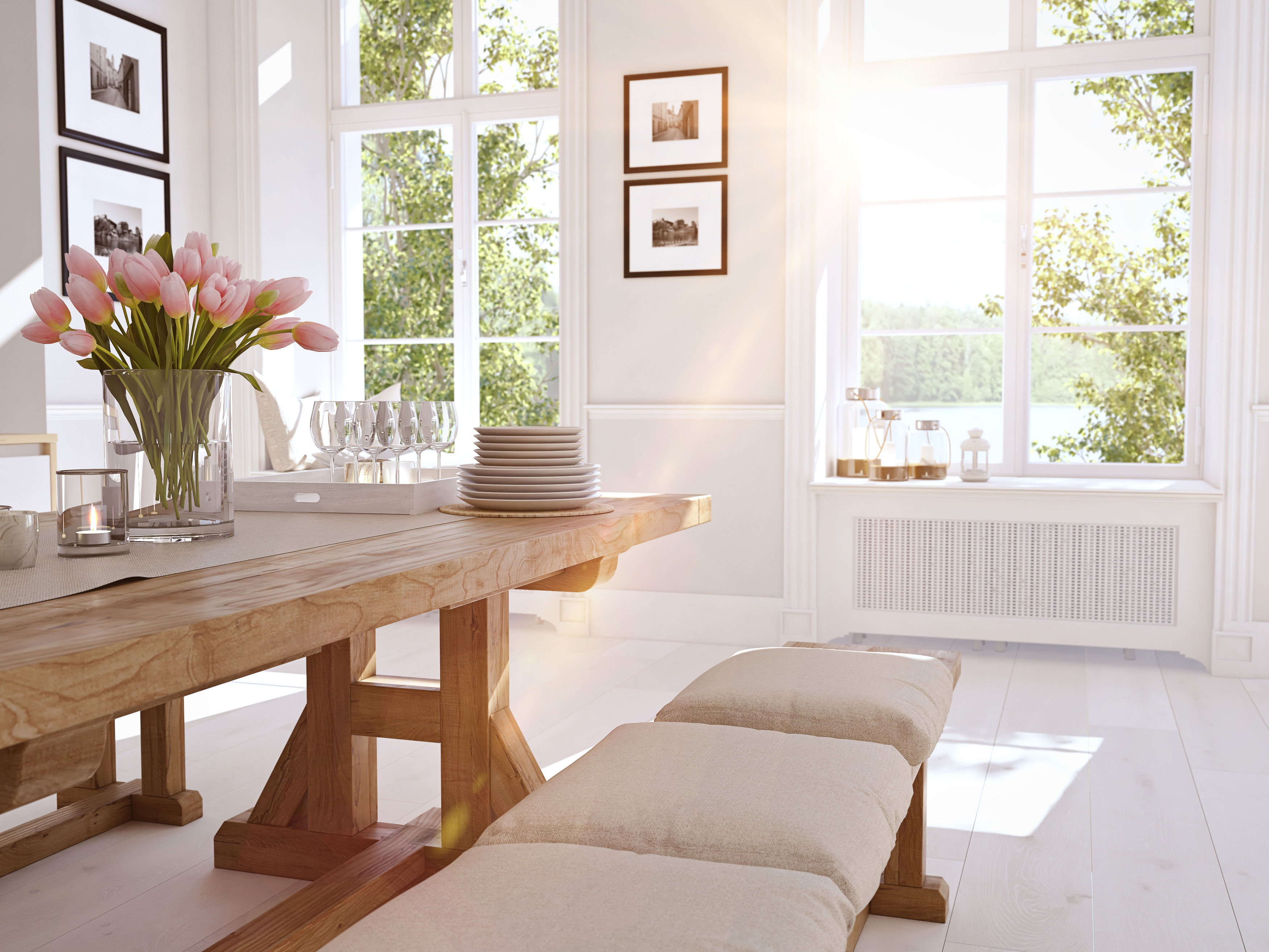 Bright dining room with wooden table, pink tulips, place settings, and large windows overlooking green foliage