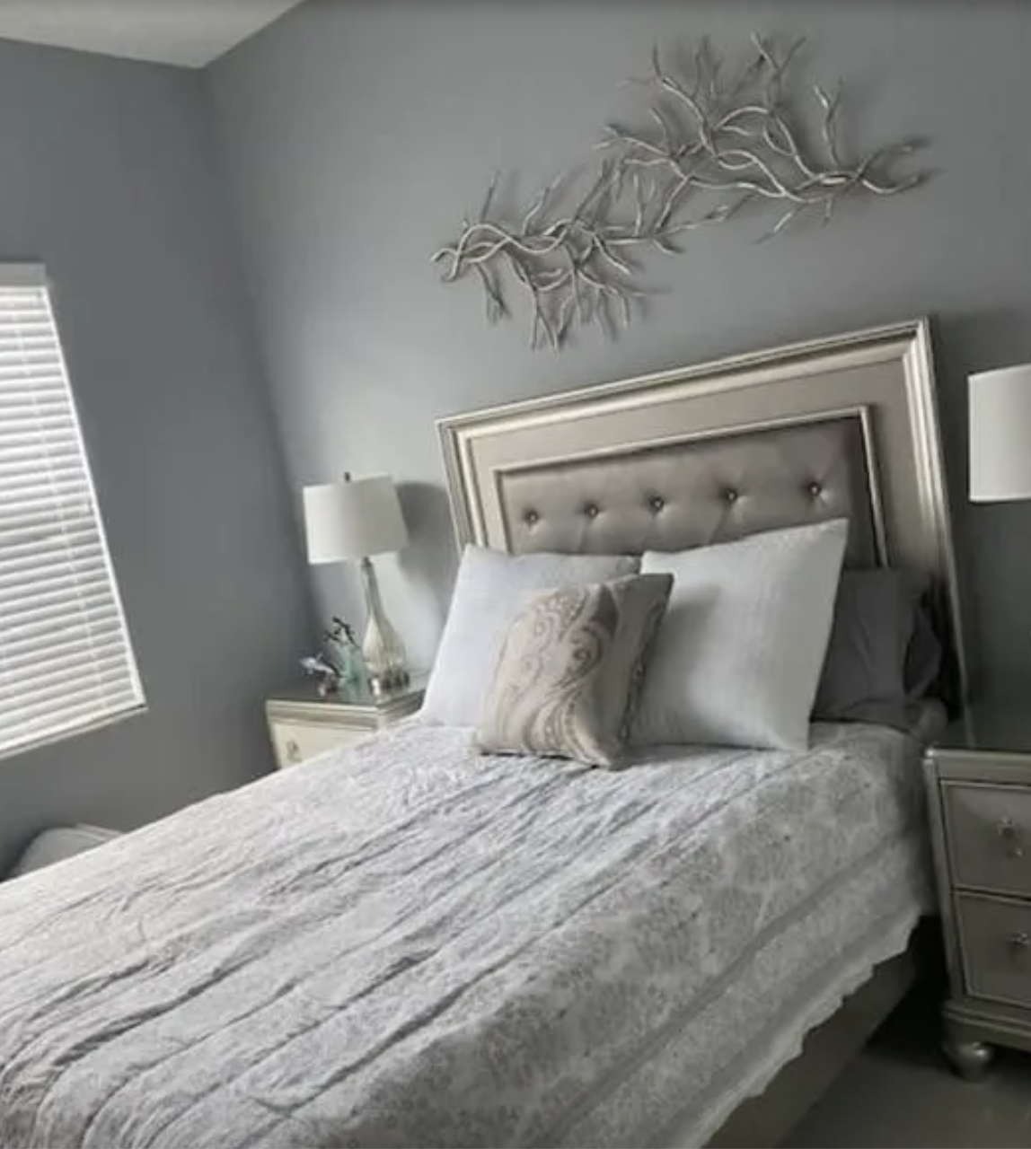 Modern bedroom with gray walls, silver-framed bed, white pillows, and decorative branch artwork above headboard