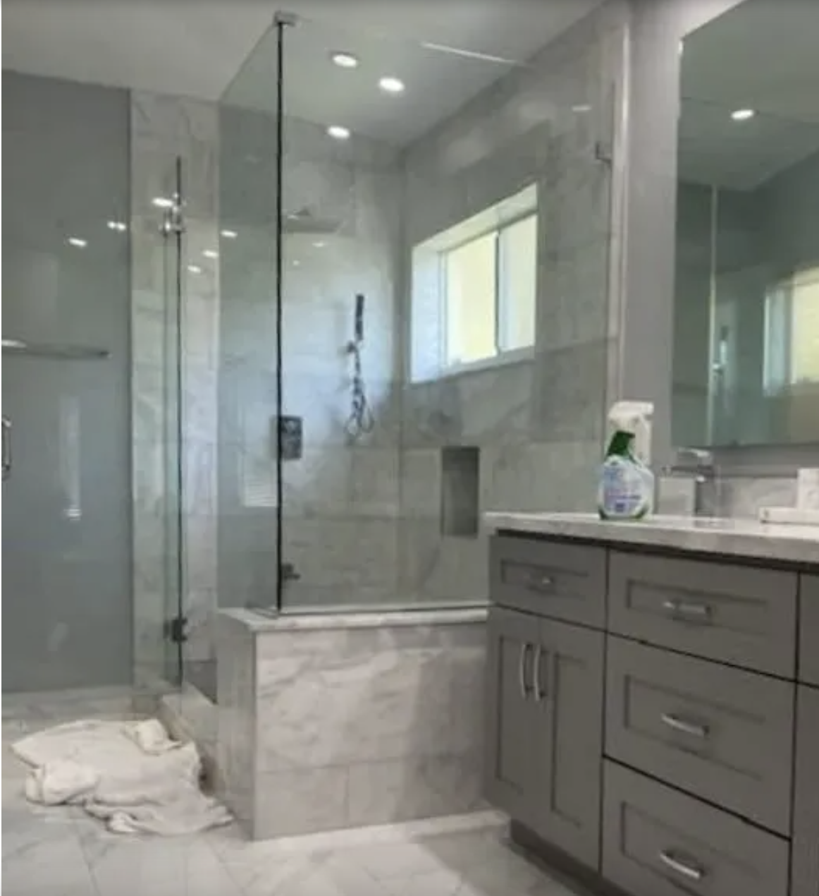 Modern bathroom with glass shower enclosure, gray vanity, and marble tile flooring